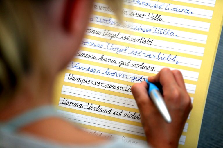 Kind schreibt Schreibschrift am Schulpult.