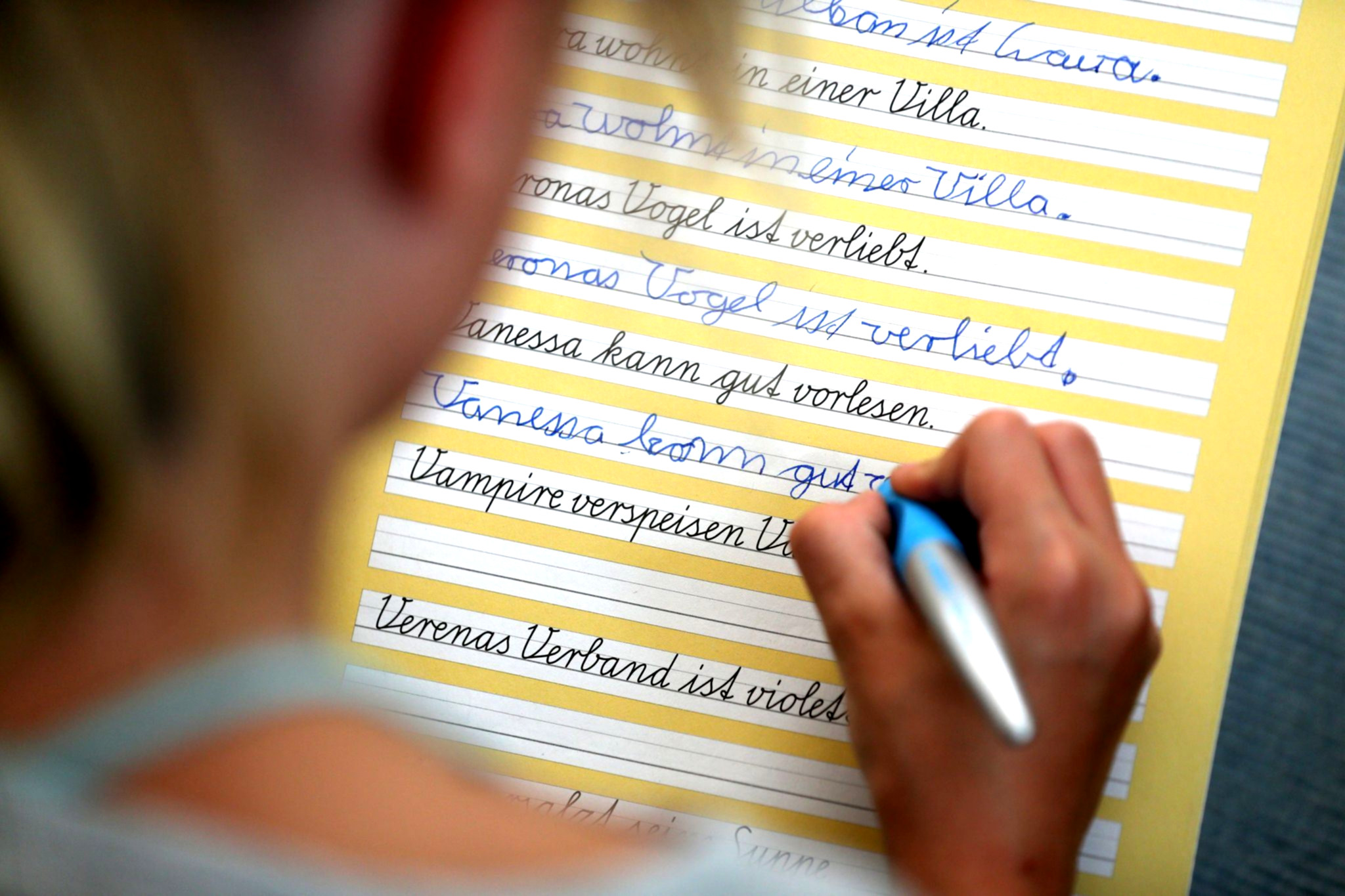 Kind schreibt Schreibschrift am Schulpult.